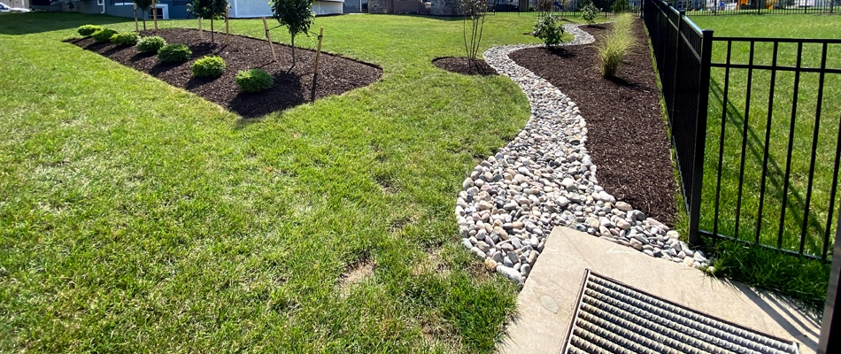 Dry creek bed along the side of a landscape bed leading to a drain.